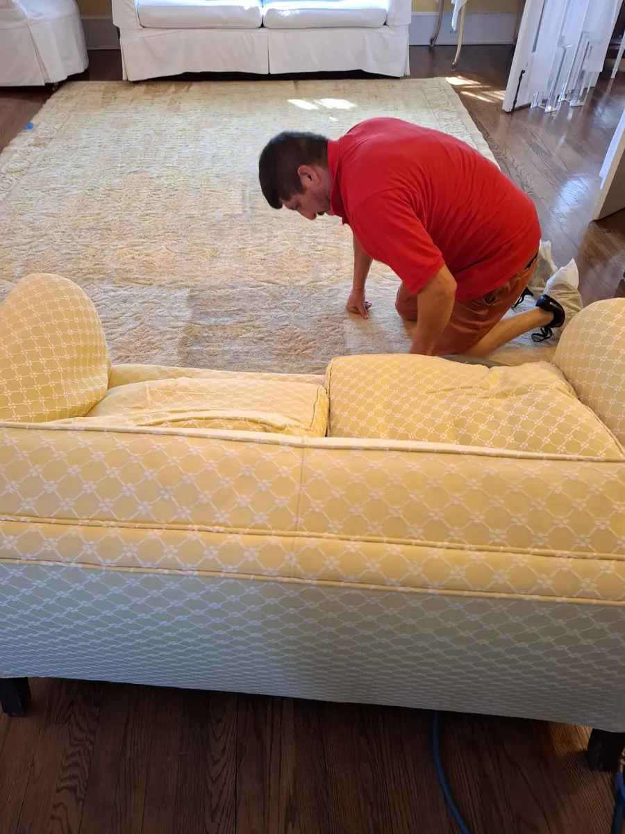 Green Choice technician cleaning a yellow patterned upholstered loveseat and wool area rug in a Long Island home